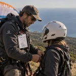 Corse parapente : moniteur ajuste un harnais pour un baptême biplace